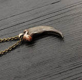 A bronze-colored canine tooth pendant necklace on a wooden surface.
